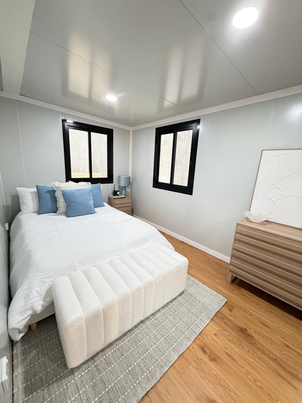 Bedroom with queen bed, black-framed sliding windows and oak-look flooring inside an Expanders® home