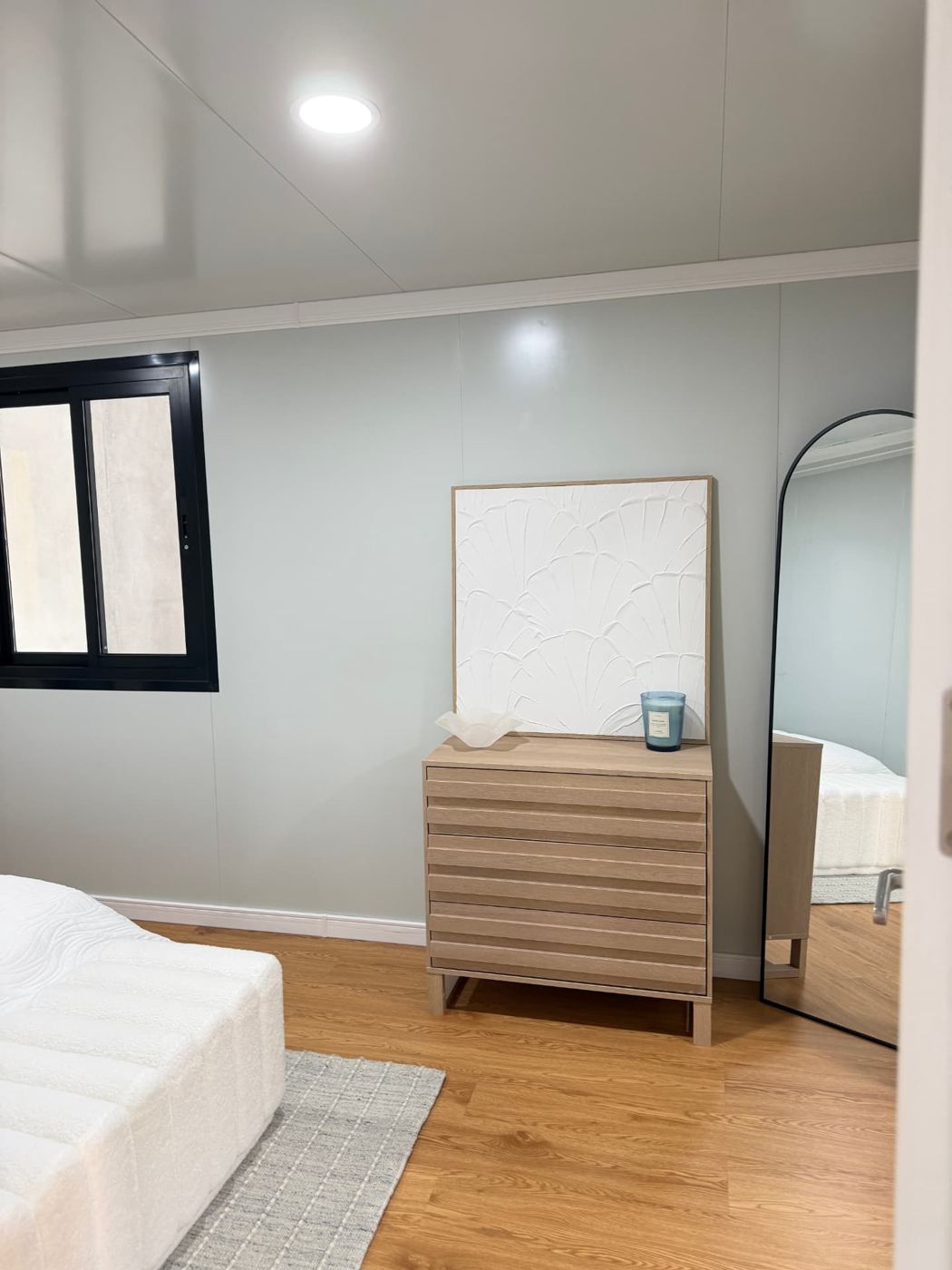 Bedroom corner with drawers, artwork and arch mirror