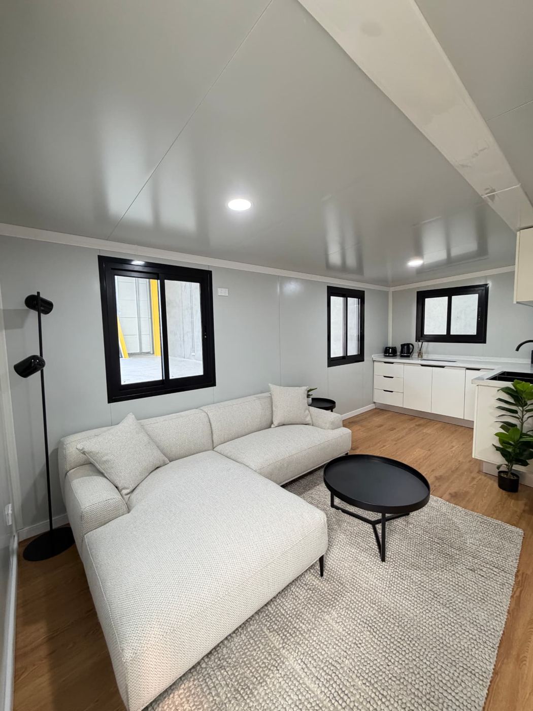 Open-plan living area with modular sofa looking through to the white kitchen inside an Expanders® home